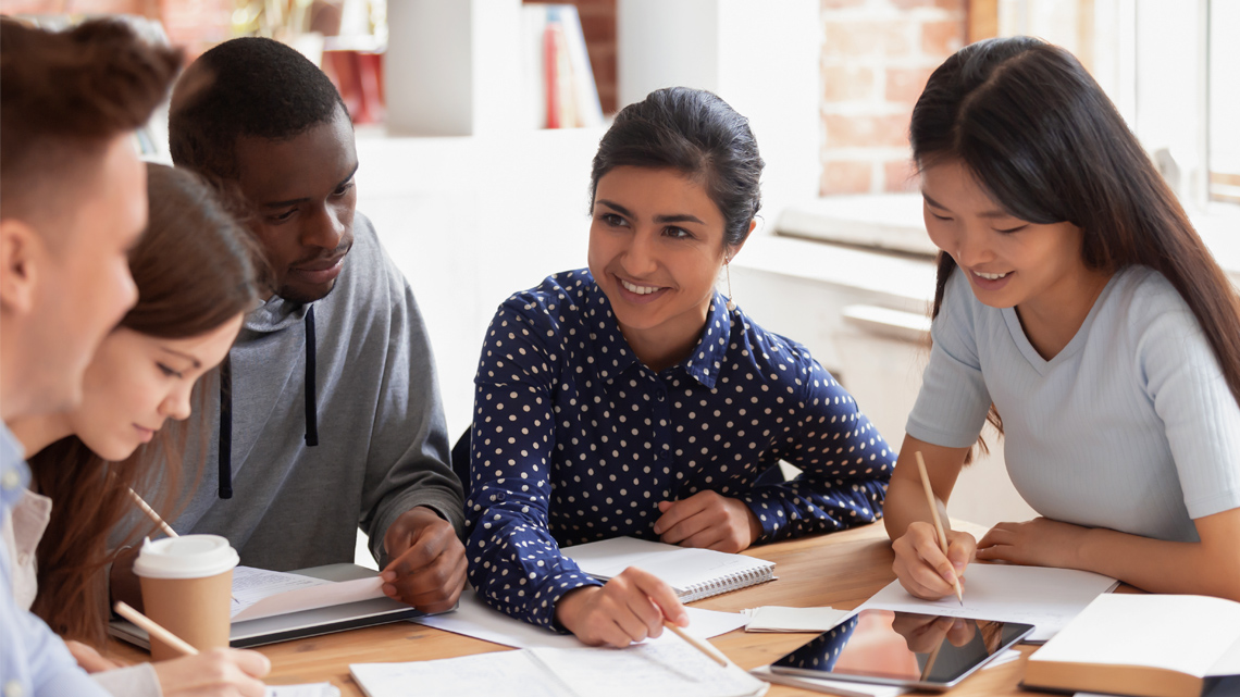 Five people gathered around a table with papers in front of them, brainstorming ideas.