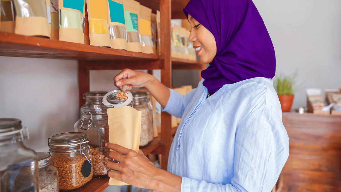 A woman in a store pouring food into sustainable packaging.