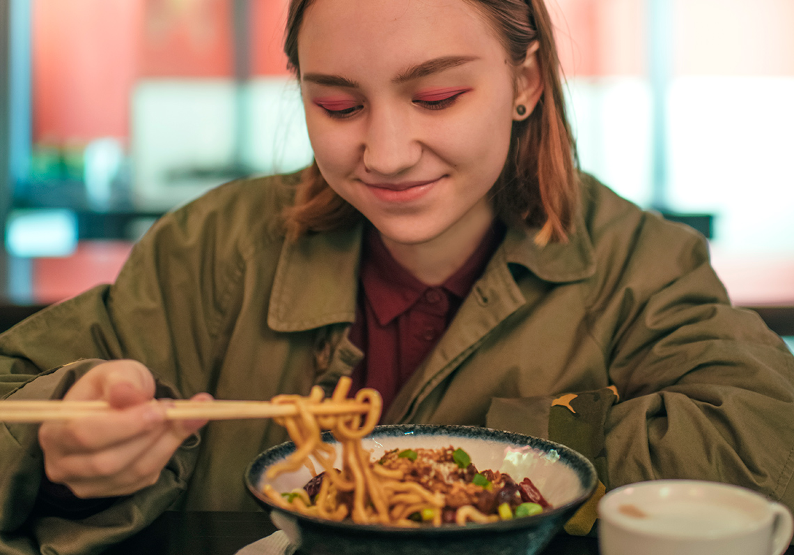 A girl eating a bowl of noodles with chopsticks