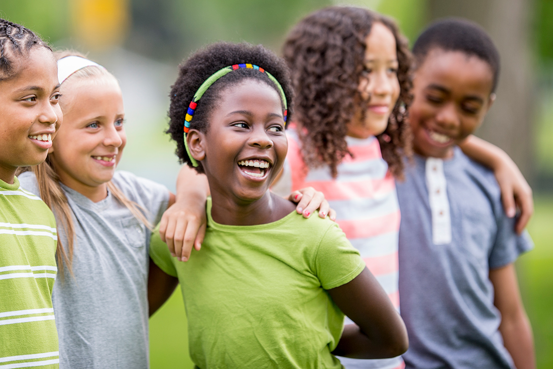 A group of kids are outside on a summer day. They are embracing and smiling
