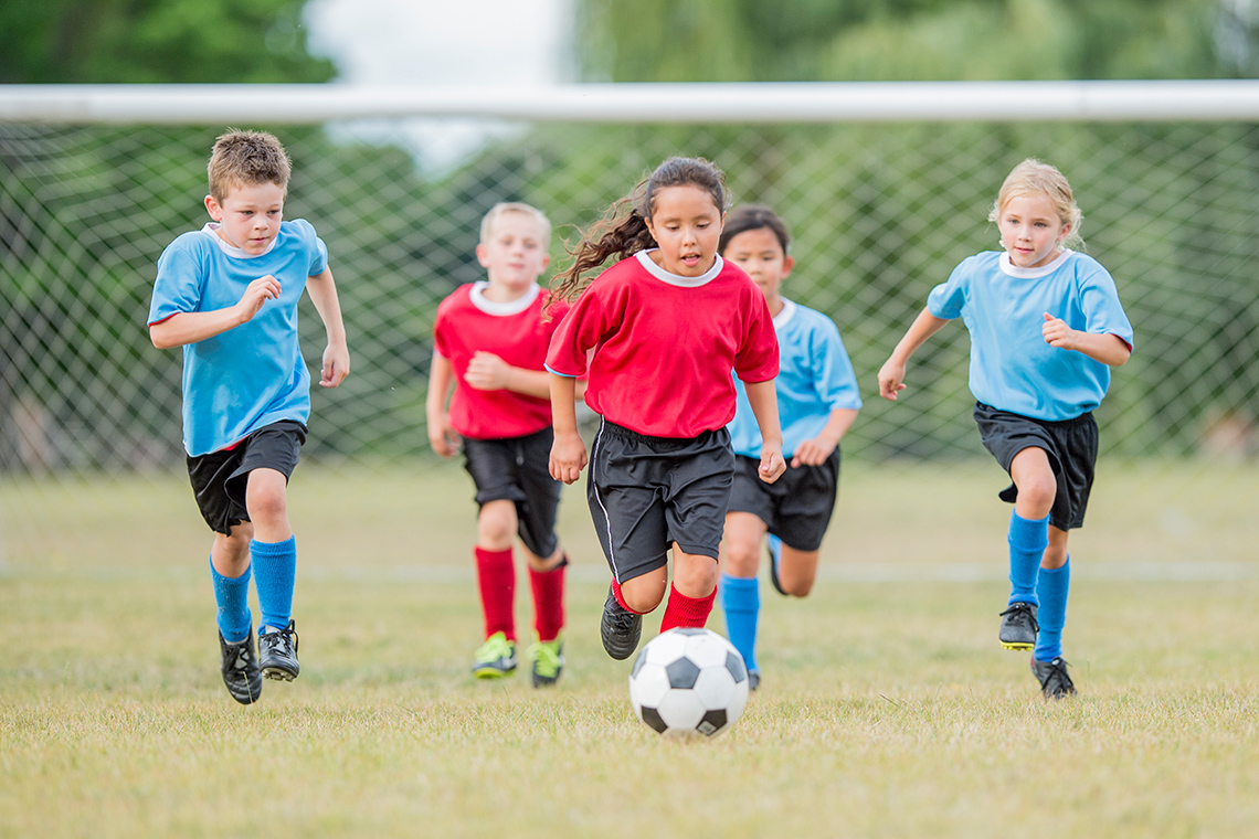 Kids in red and blue uniforms are playing soccer