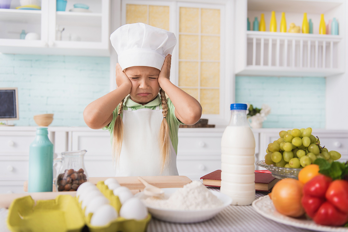 A sad chef in uniform sitting on floor in a kitchen and looking away