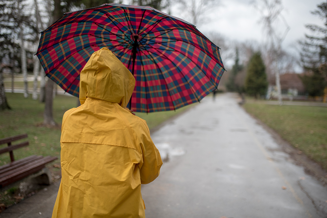 A person in a yellow raincoat holds an umbrella and walks in the park