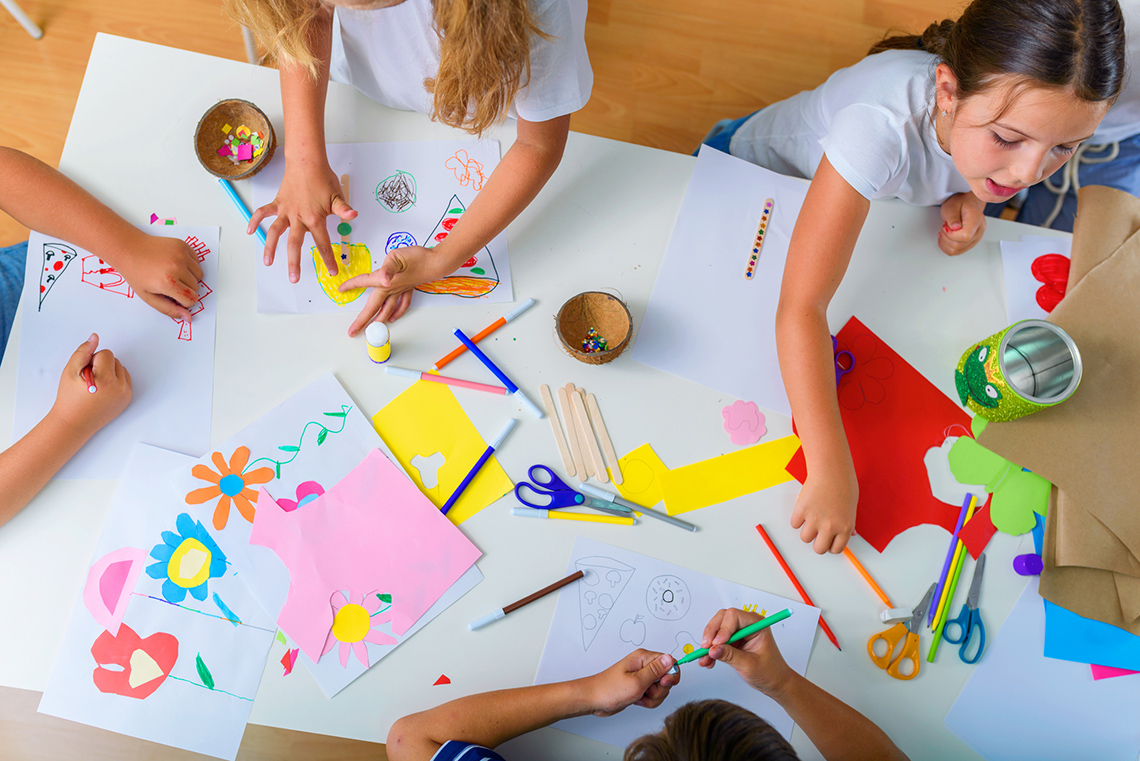 Children around a table with papers, scissors and coloured pens, creating flowers and drawing