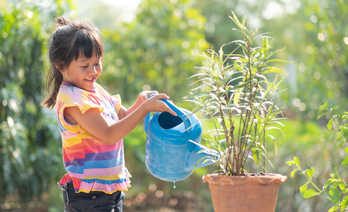A young child pours water from a watering can.