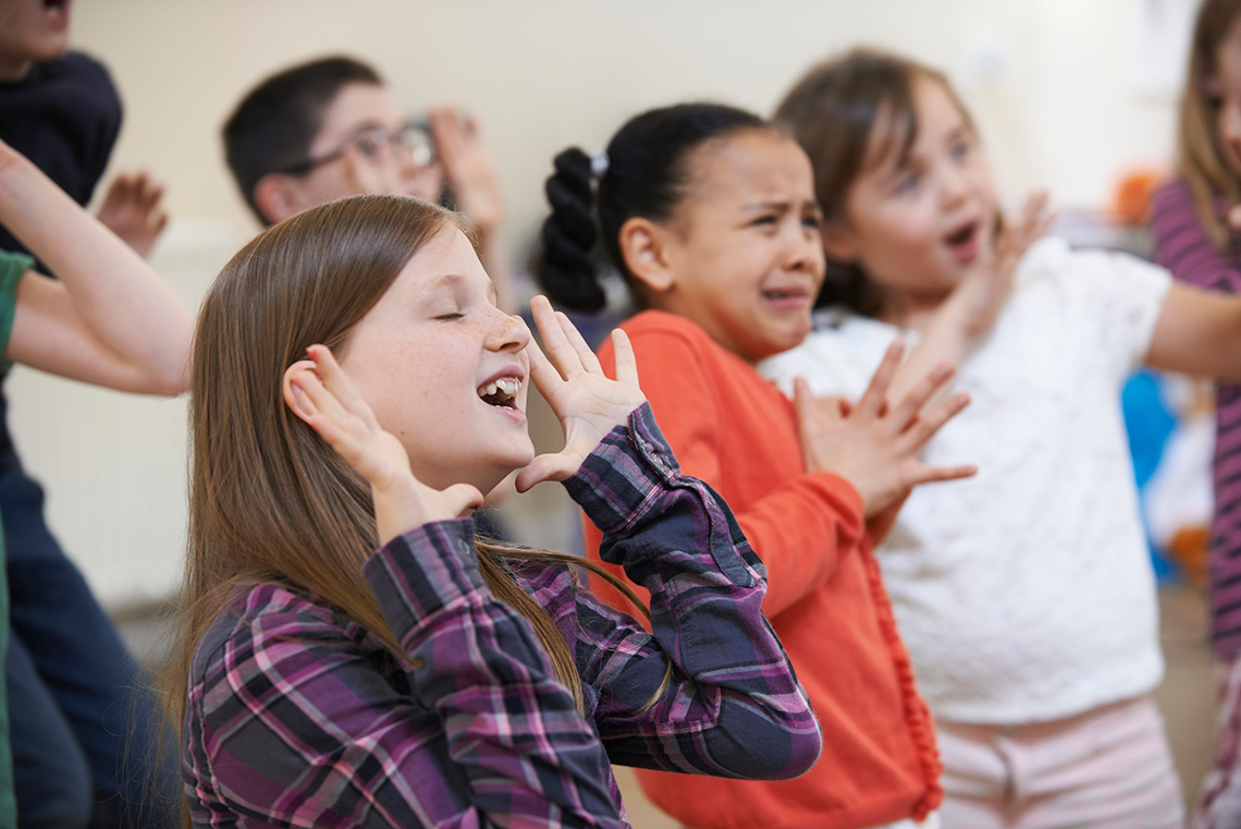 Four young students spread their fingers next to their faces with their eyes and mouth opened wide.