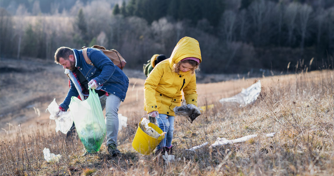An adult and child are cleaning up litter from a field.