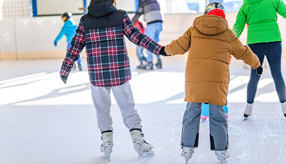 This is a colour image of children ice skating together and holding hands.