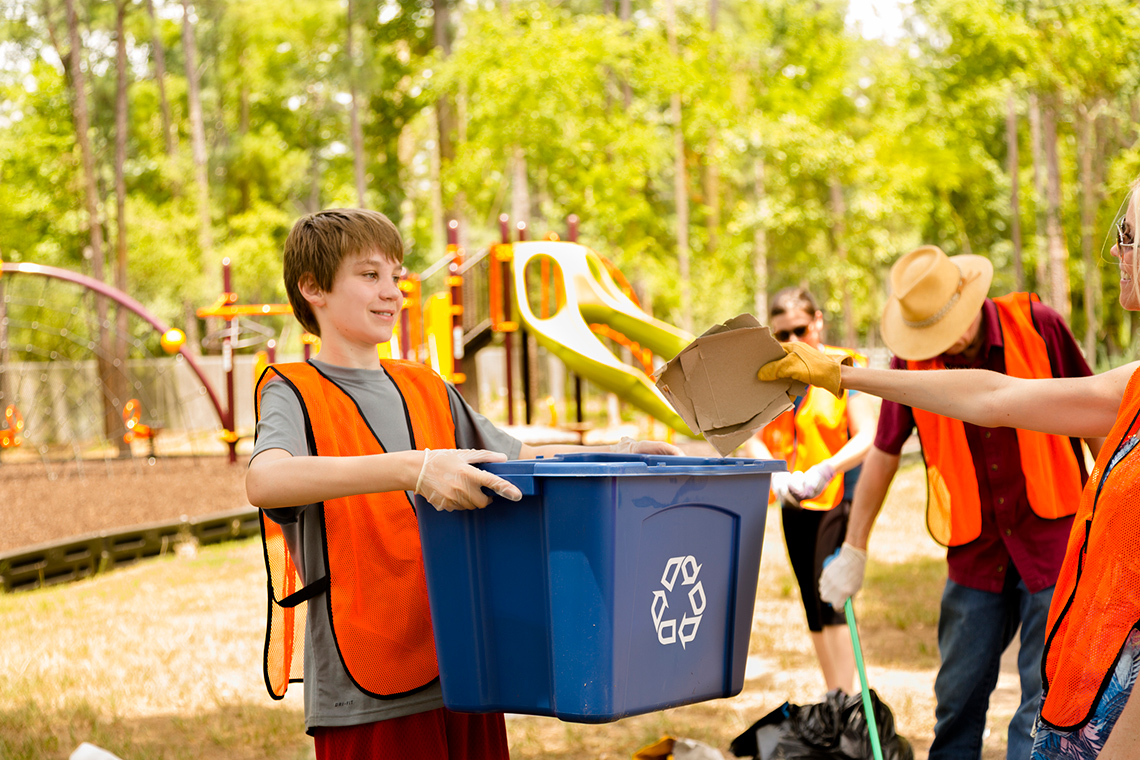 Two young students wearing rubber gloves and picking up plastic water bottles in their neighbourhood pathway.