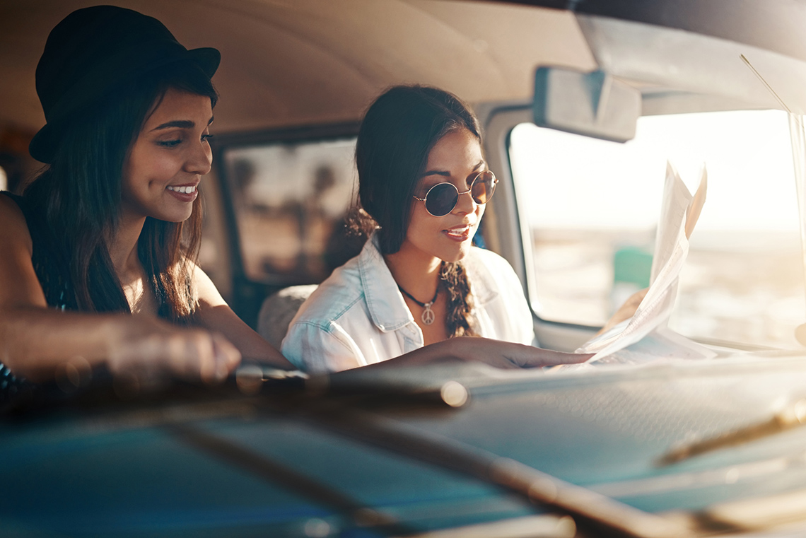 Two friends in the front seat of a vehicle and focusing their attention on a map.