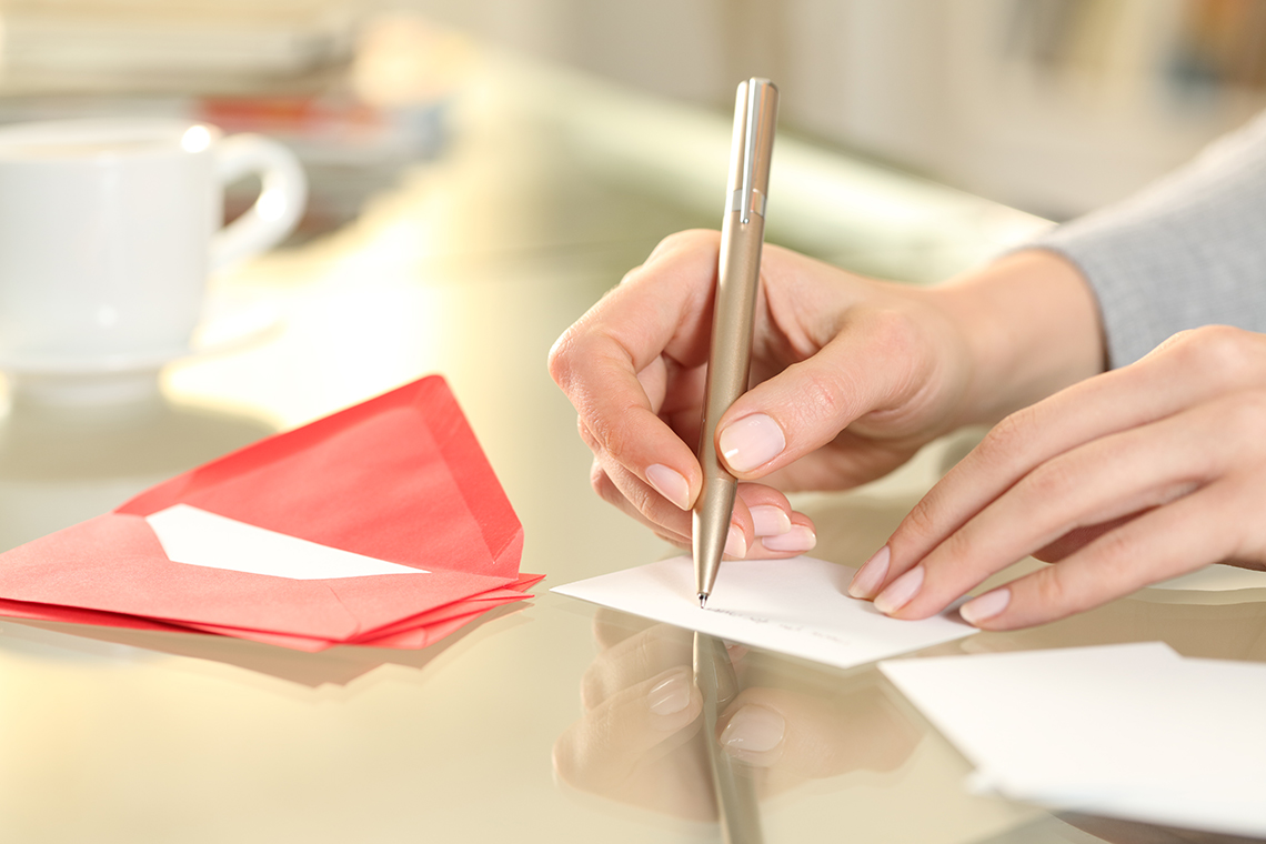 Someone writes on a card with a pen, with red envelopes and a teacup shown close by.