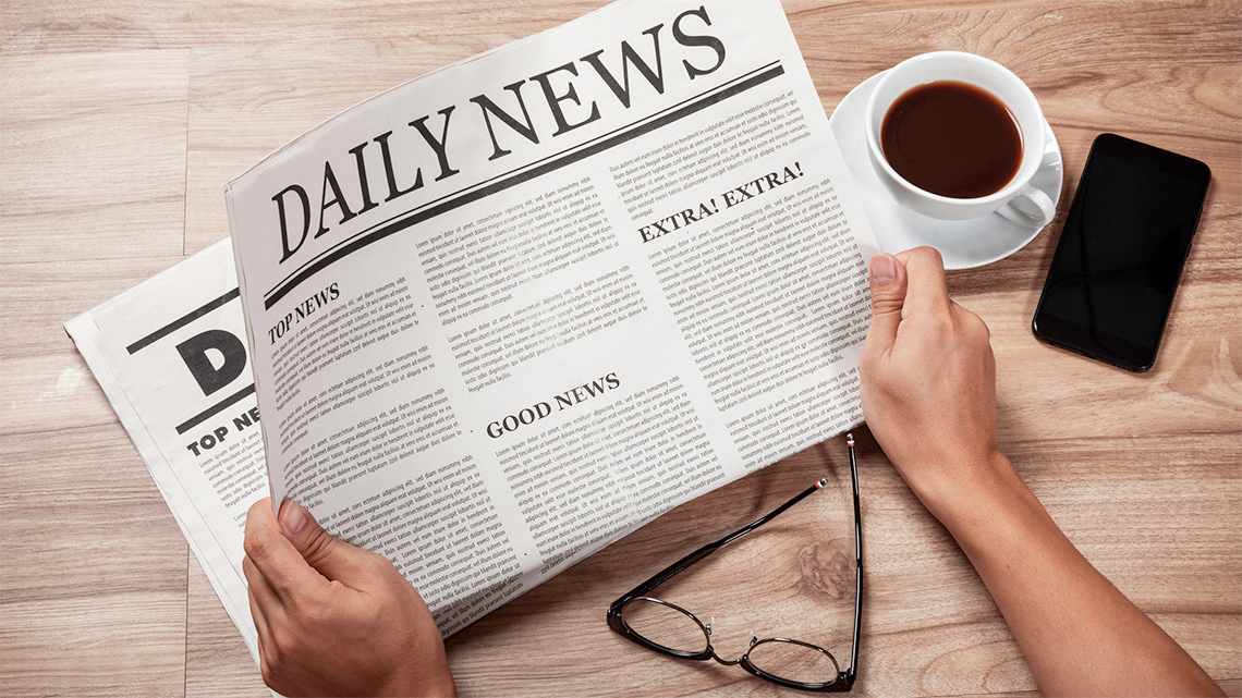 Hands holding printed “Daily News” newspaper with many articles.