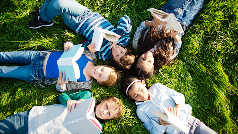 Aerial view of a group of students laying in the grass in a circle and reading.