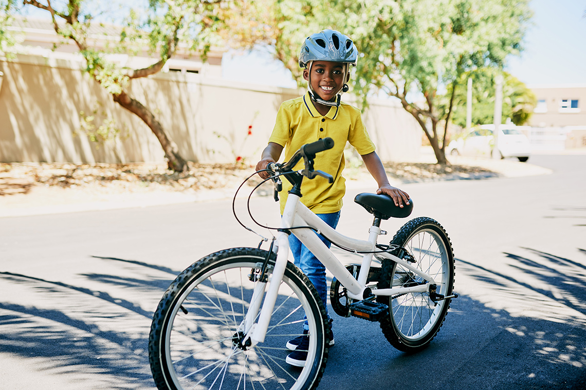 A young boy with a yellow shirt standing next to his white bike.