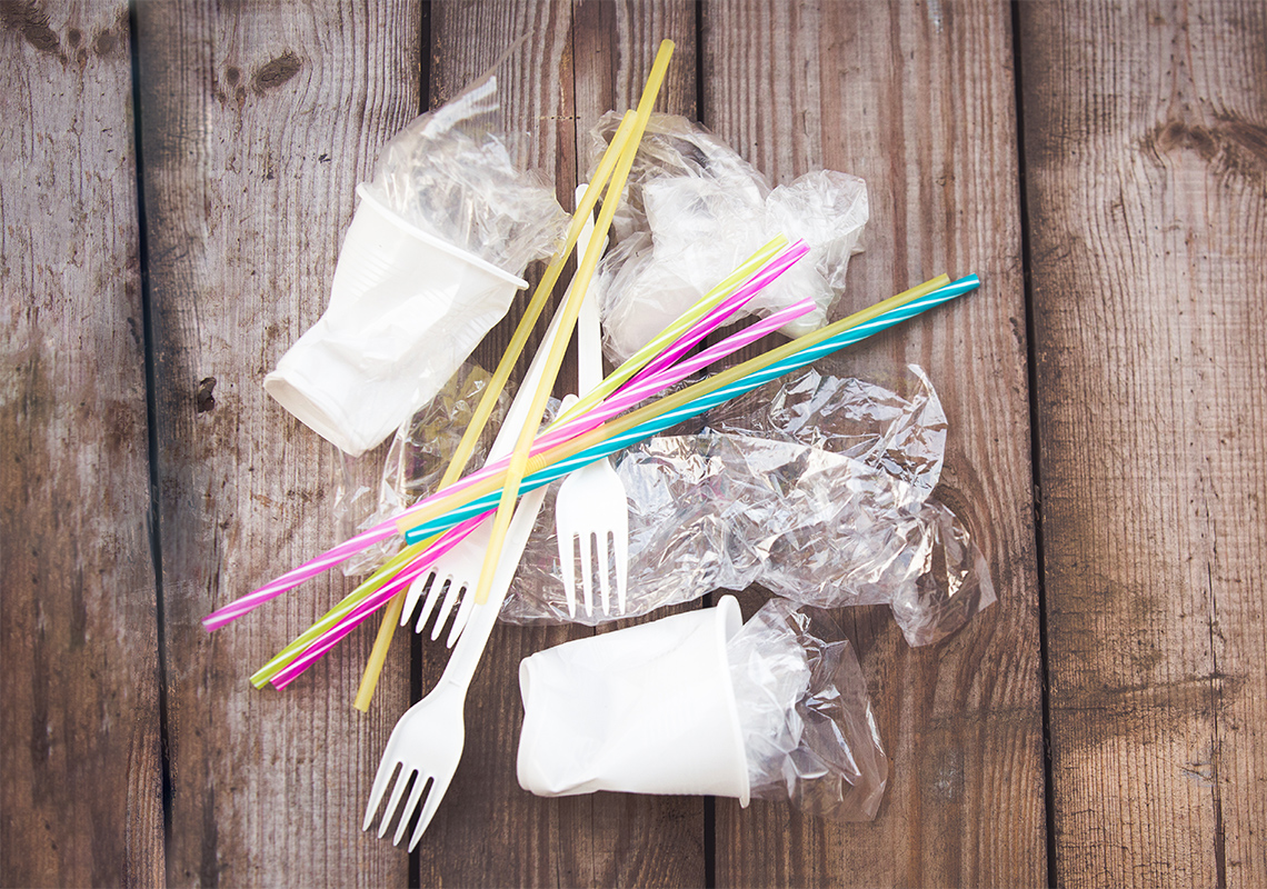 There is a pile of plastic forks, bags, cups and straws. 