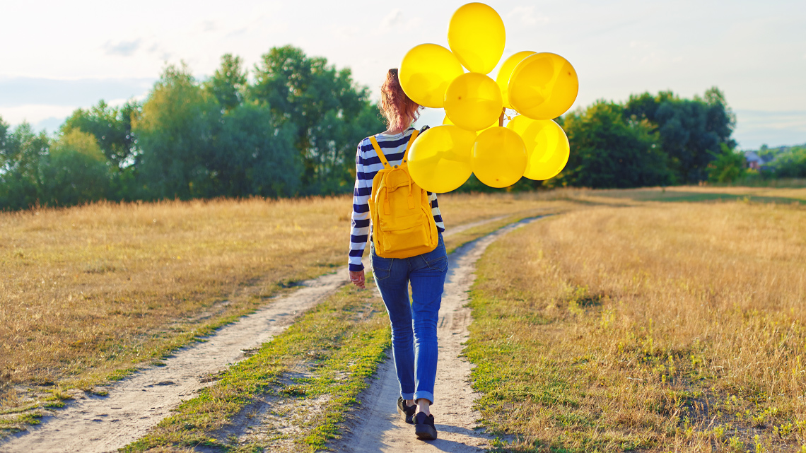 A girl is walking towards the horizon holding a group of balloons