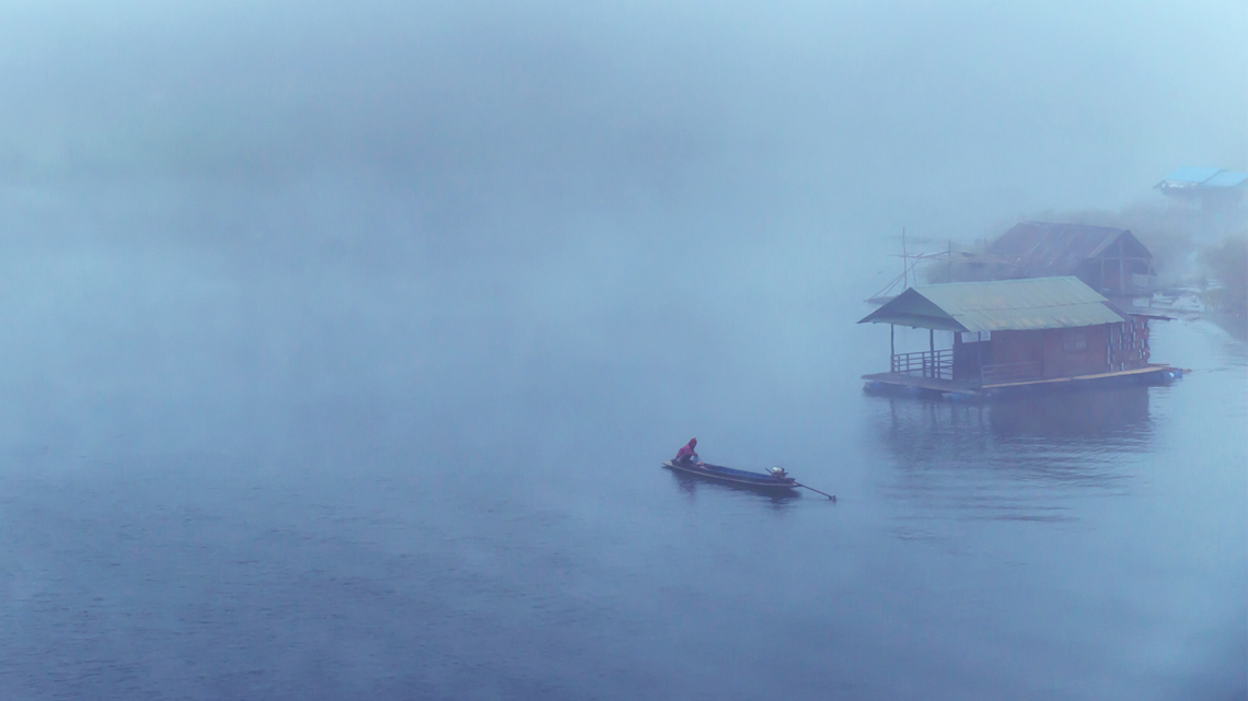 Two people in the foggy distance canoeing on the lake
