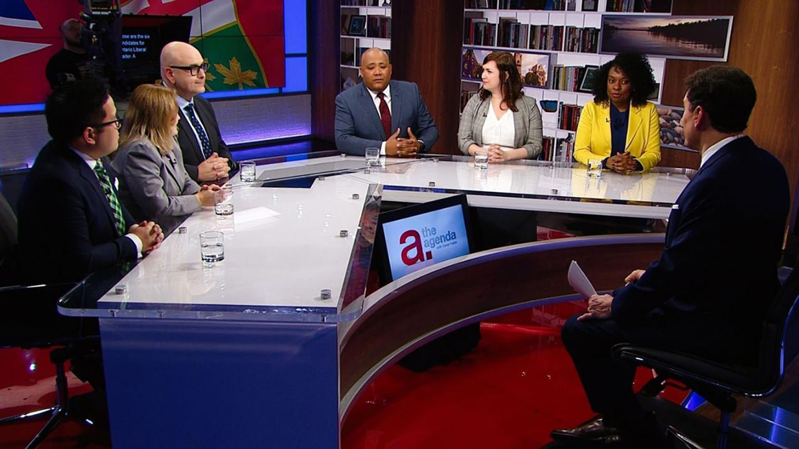 People seated around a desk on a TV set.