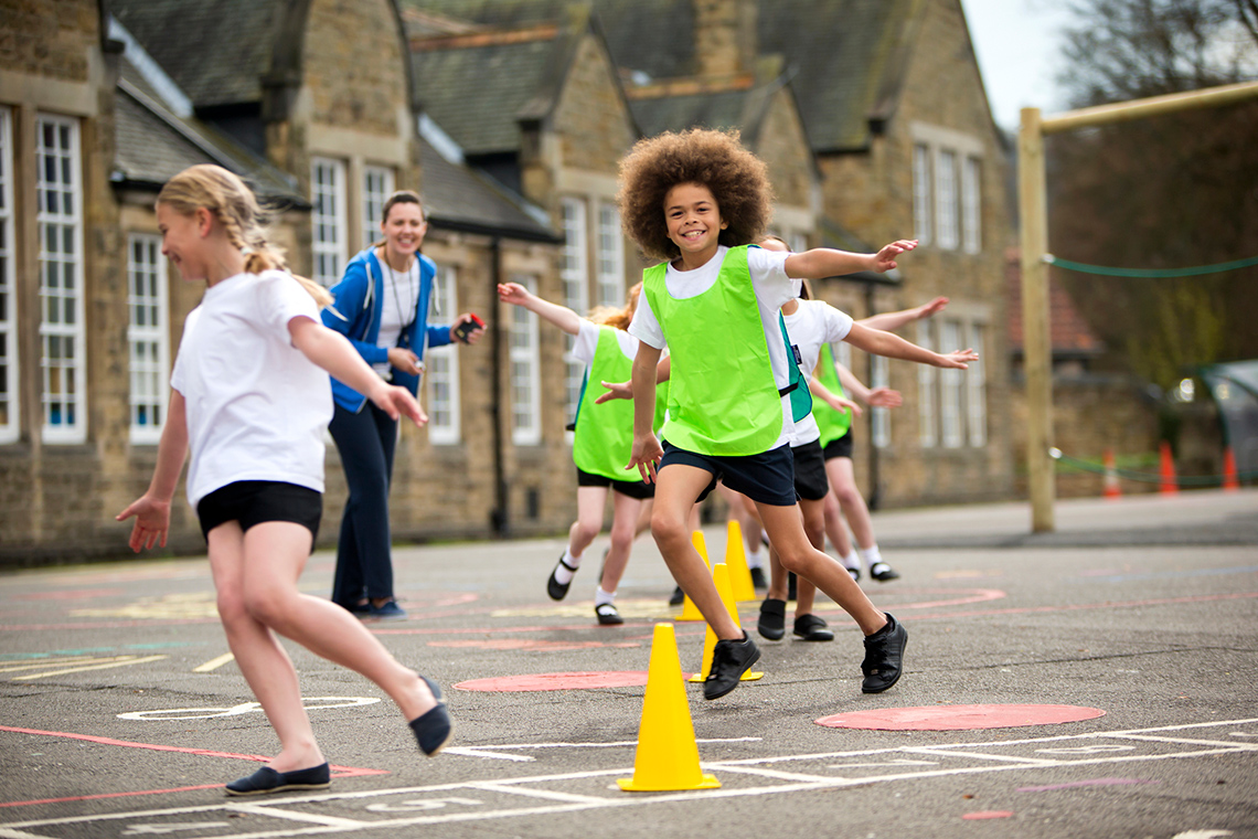 Children running outside around obstacles like pylons.