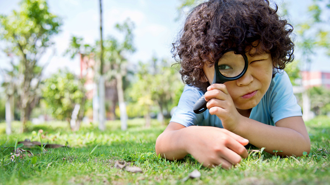 Child searching outside with a magnifying glass.