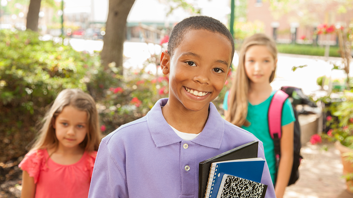 A group of young students wearing backpacks as they walk across a crosswalk.