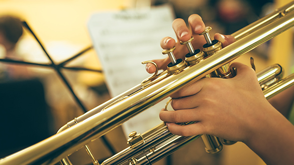 Close up of a child’s hands playing the trumpet in a music class.