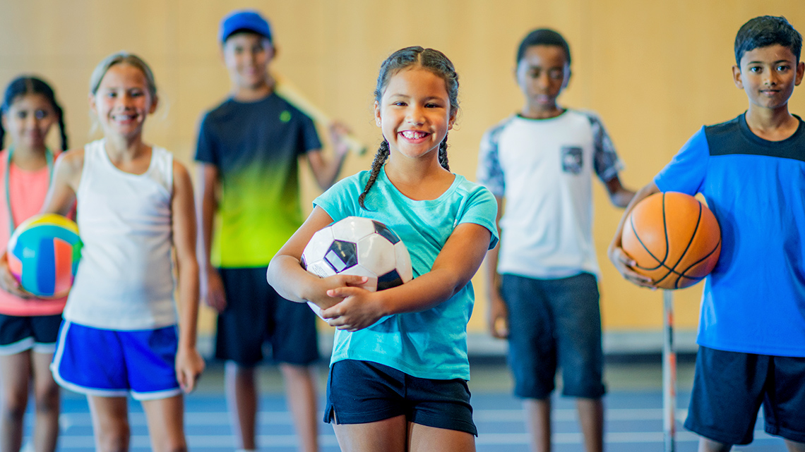 Favourite Sports A group of students stand and smile while holding different sports equipment.