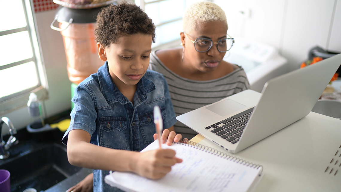 An image of a student and an adult doing research on a laptop from home.