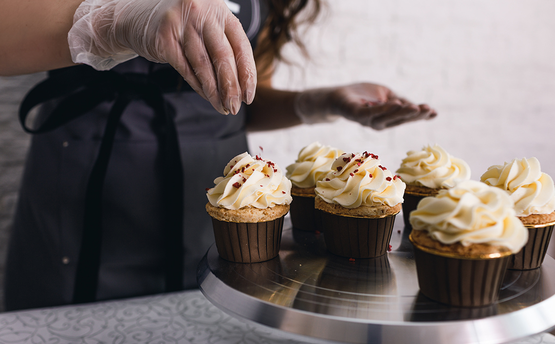 Cupcakes An image of a baker putting sprinkles on cupcakes topped with vanilla cream.
