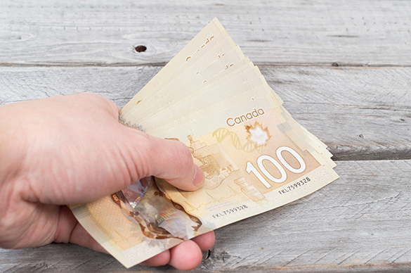 Person holding a bundle of 100 Canadian dollars in their hand.