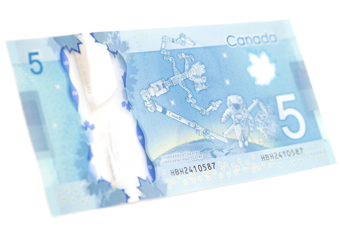 The back of a Canadian 5 dollar bill. The bill has the number 5 and a picture of a robotic arm and an astronaut in space.