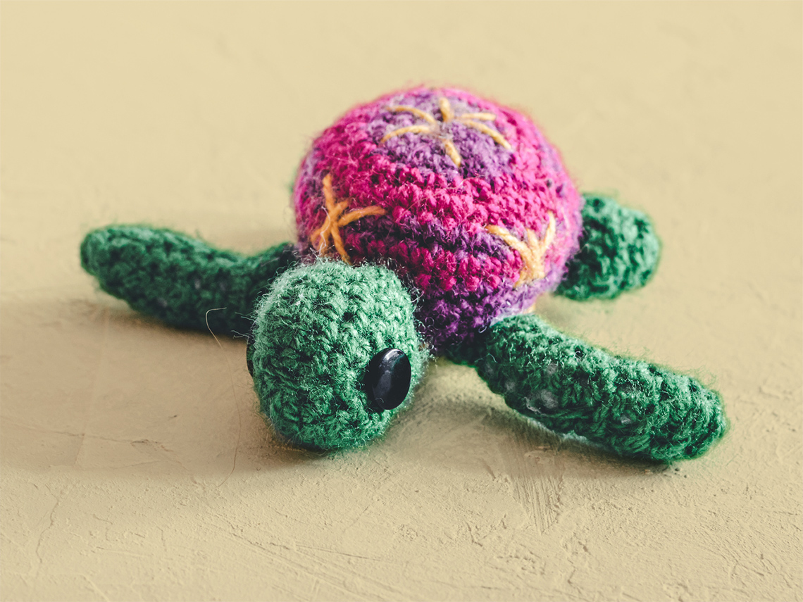 A stuffed animal turtle made using crochet. It has different colours and patterns on its shell.