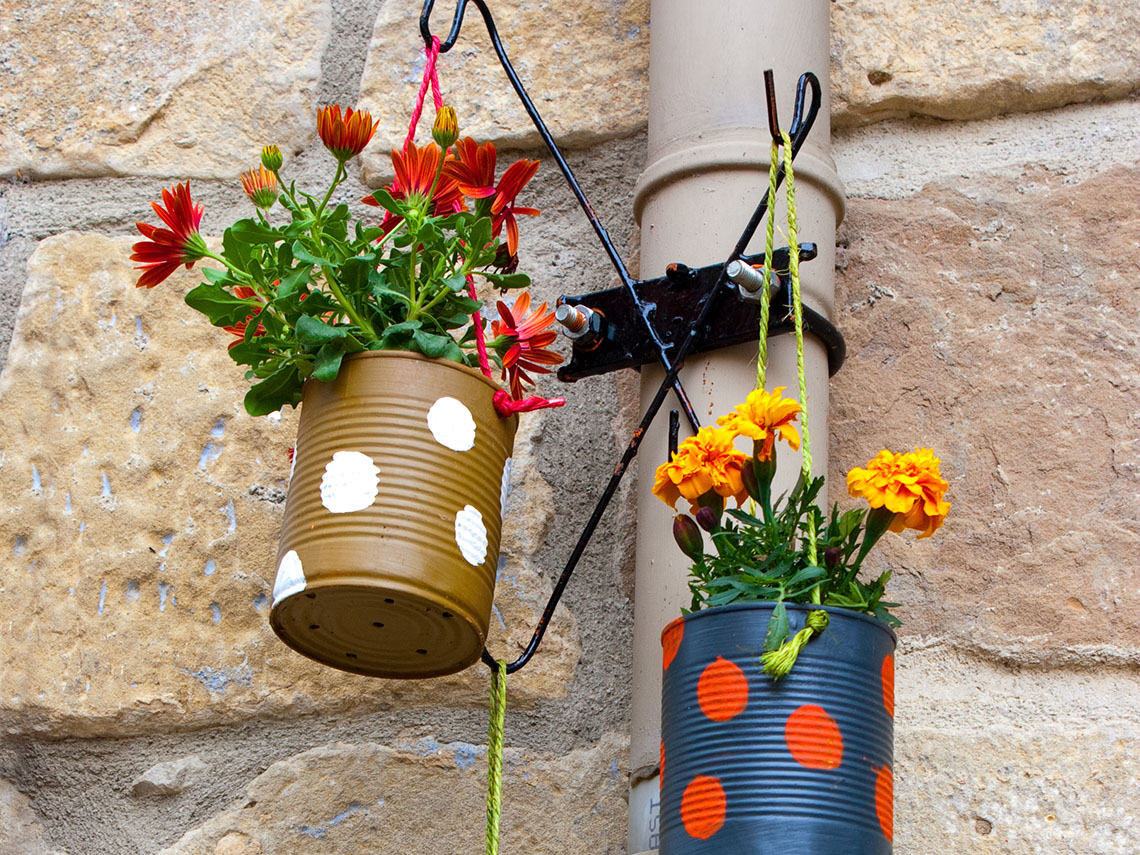 Three cans painted with colourful polka dots hanging from a metal stand. Each is filled with flowers. 