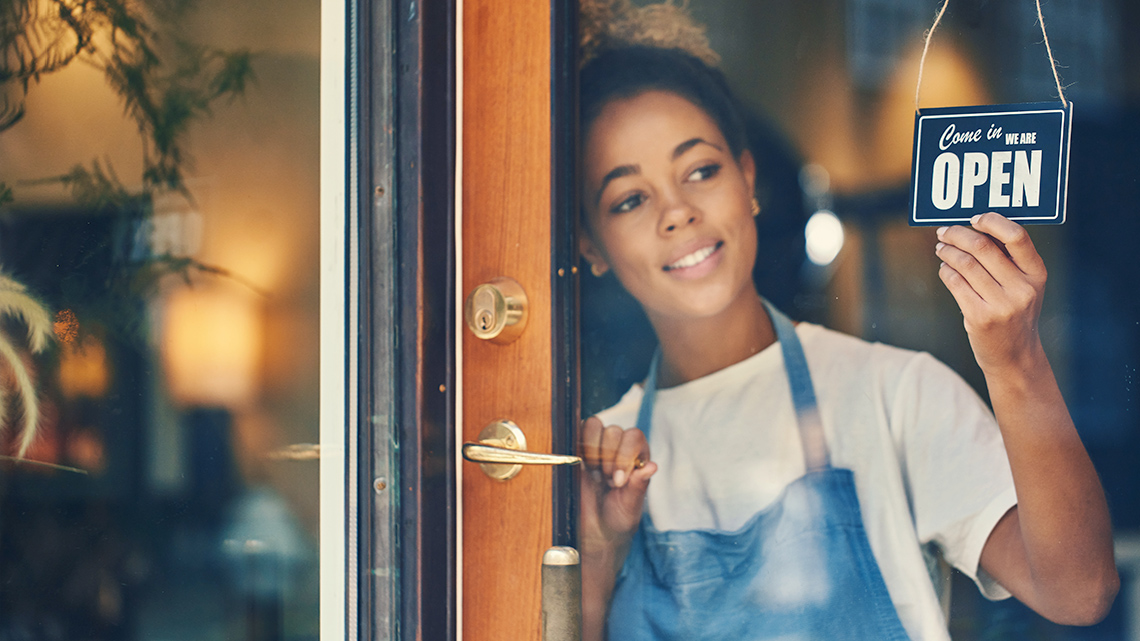 A woman hanging up a sign in a business saying they are open.