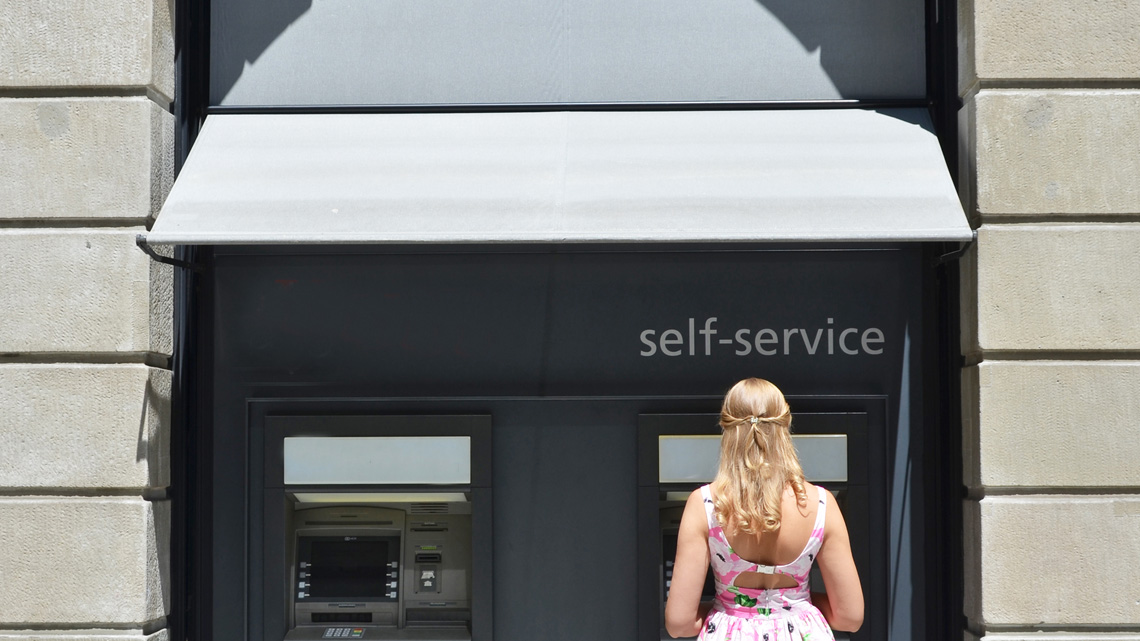 Woman outside of a bank using a bank machine.