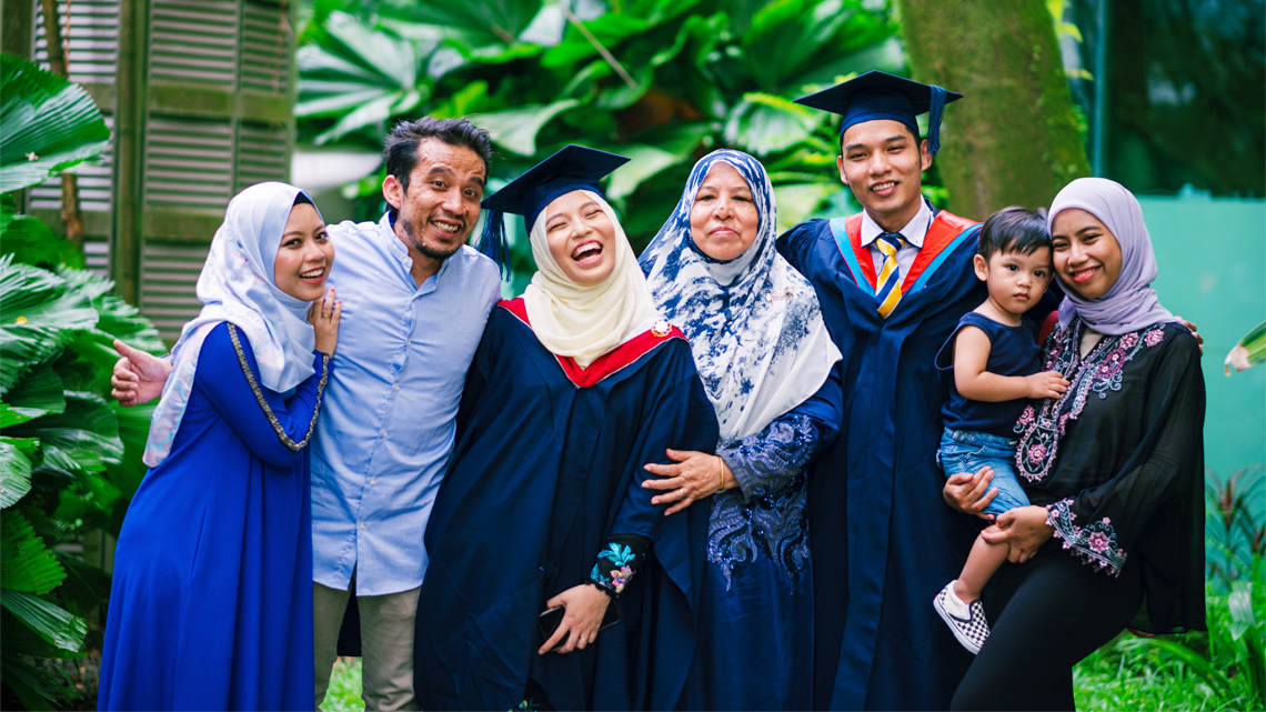 Seven family members smiling during a graduation ceremony. The mother of the graduates is in the centre.