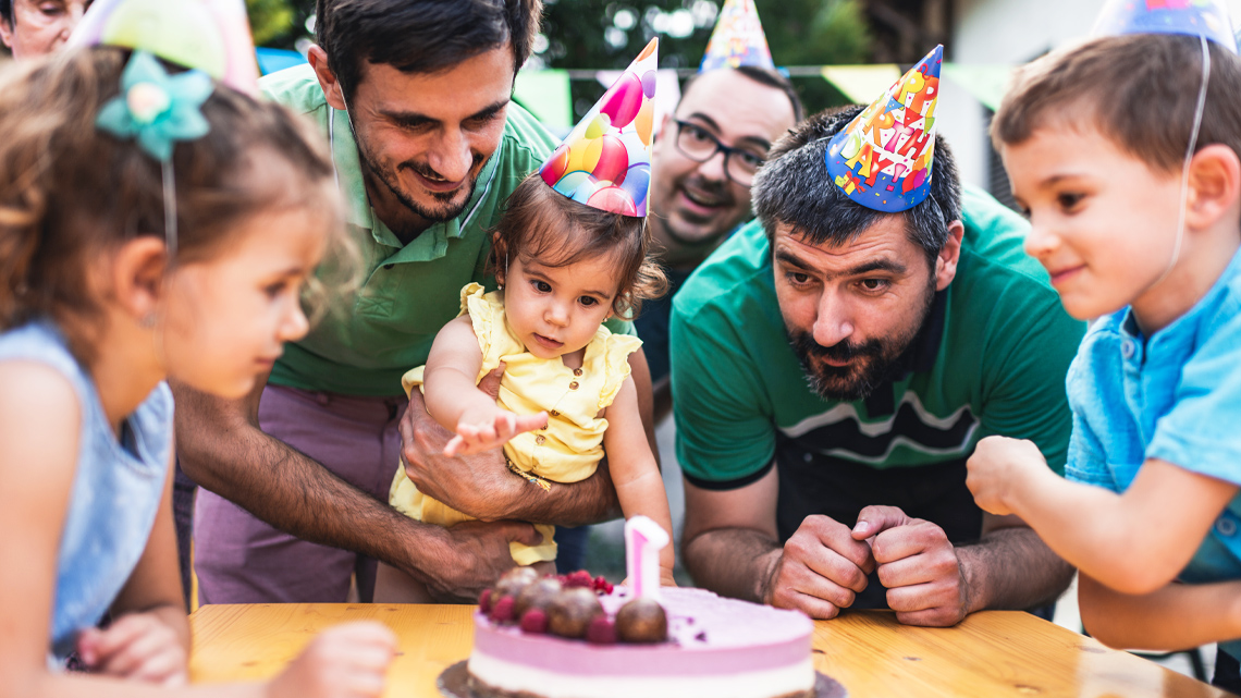 Seven family members at a birthday party. At the centre are two fathers and their child.