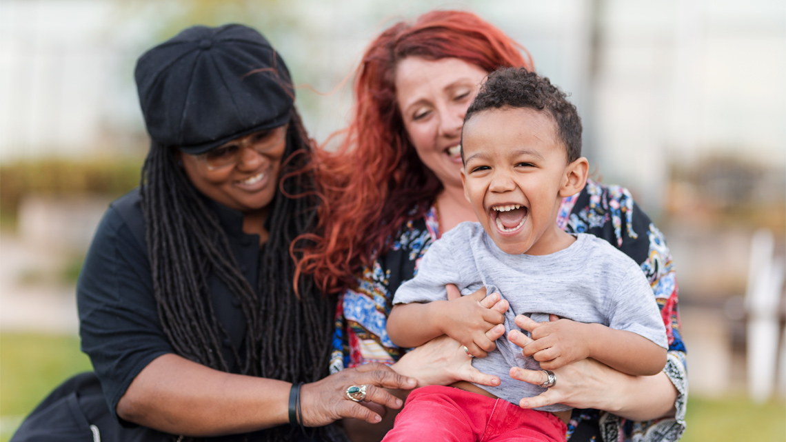 Three family members, two mothers and one child smiling at the camera.