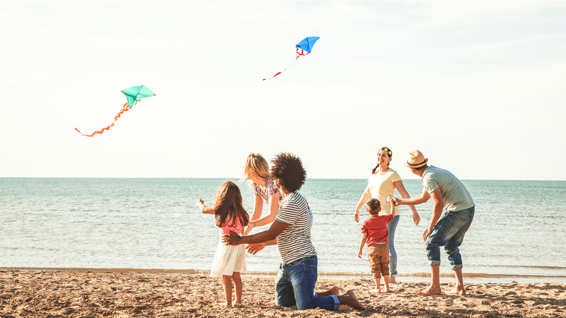 Six family members flying kites in the beach, helped by a mother and father.