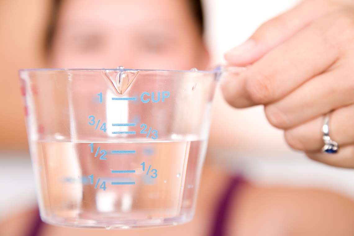 Hand holding a measuring cup filled with water close to 2/3 mark. Measures shown are: 1 cup, 3/4, 2/3, 1/2, 1/3 and 1/4.