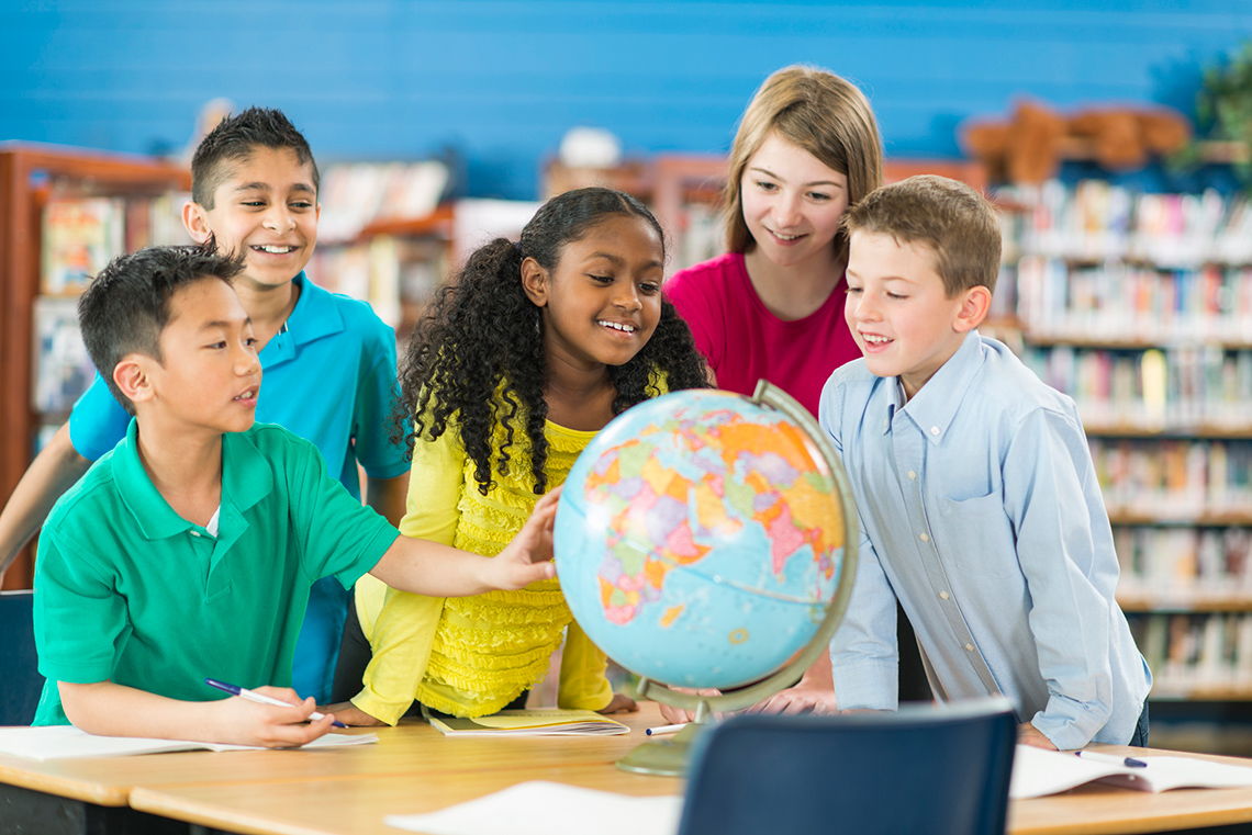 Children Exploring the Globe Children gathered around a globe in the classroom.