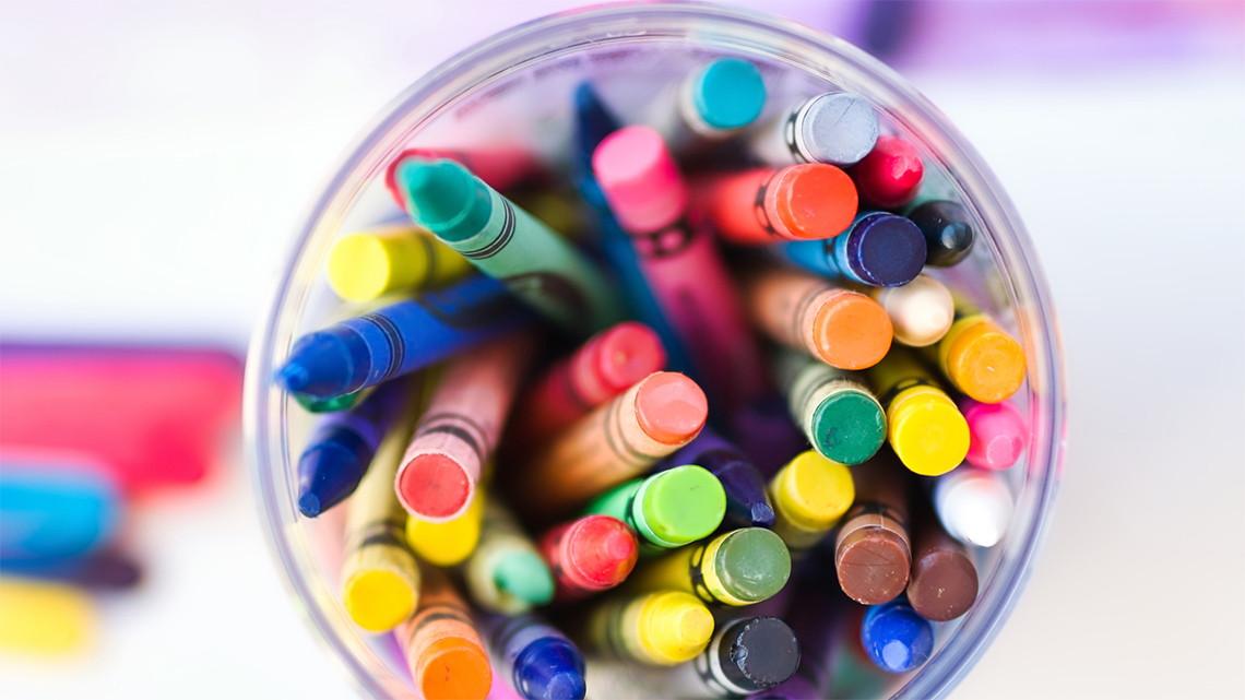 Clear cup filled with colourful crayons.