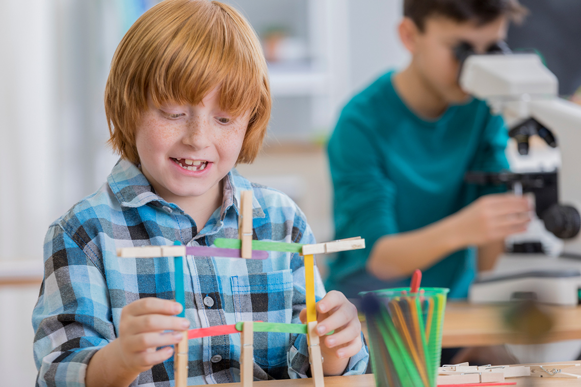 Student using colourful popsicle sticks and clips to create a four sided shape in the classroom.