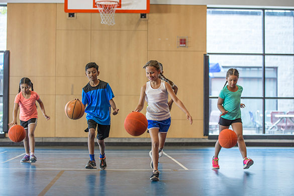 Children bouncing basketballs in a gym.