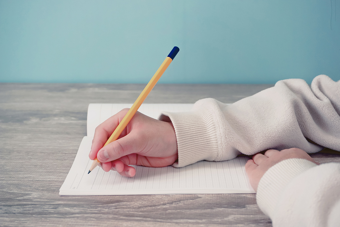 Closeup image of a hand, writing with a pencil in a notebook.