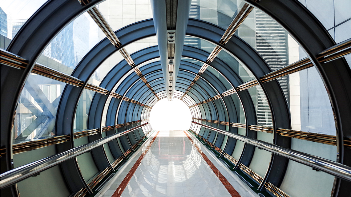 A straight walkway through a round tunnel with windows. The are metal support pieces around the circle and along the length.