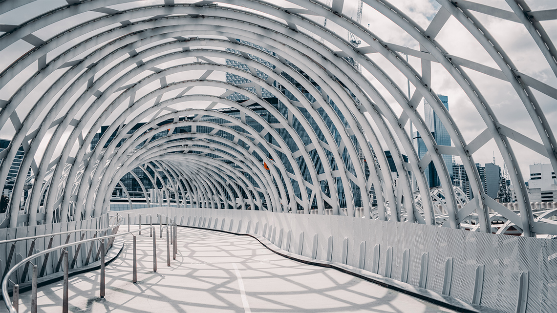 A curving walkway through a round tunnel with windows. Metal support pieces are at angles around the outside of the tunnel.