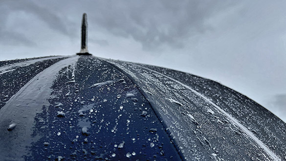 The top of an open umbrella that is wet from heavy rain is shown with dark storm clouds in the background.