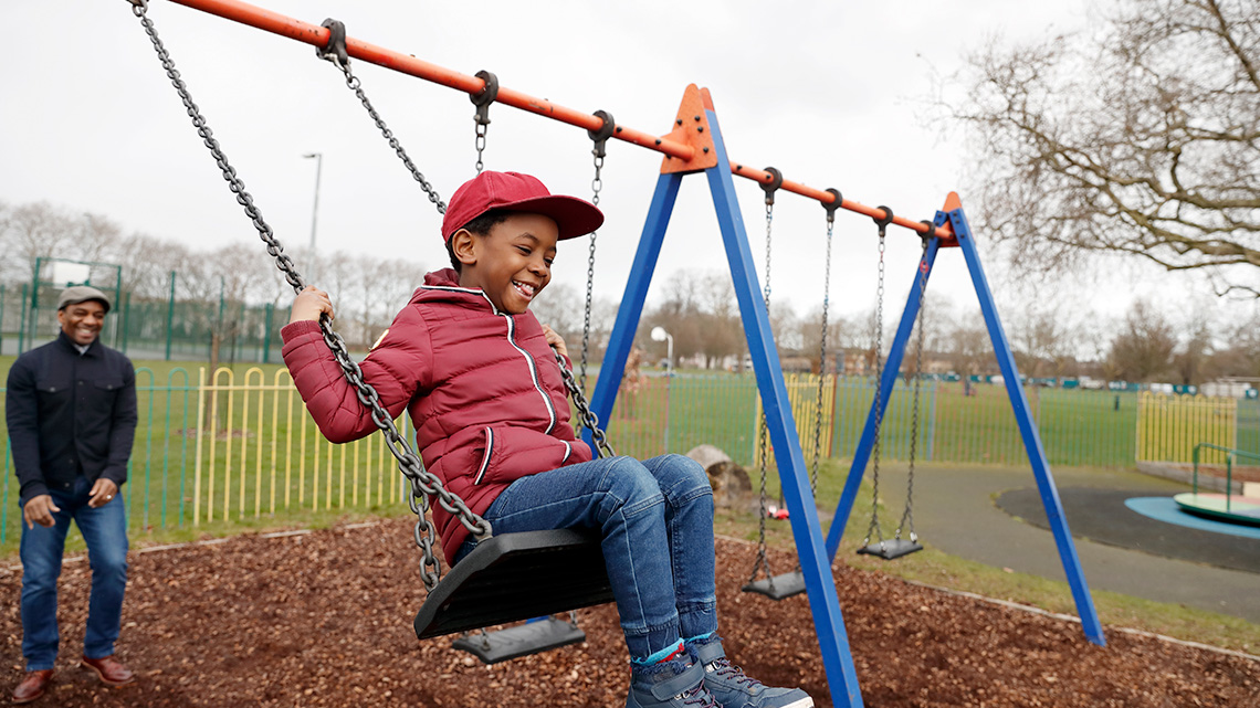 A guardian pushing a child on a playground swing set.