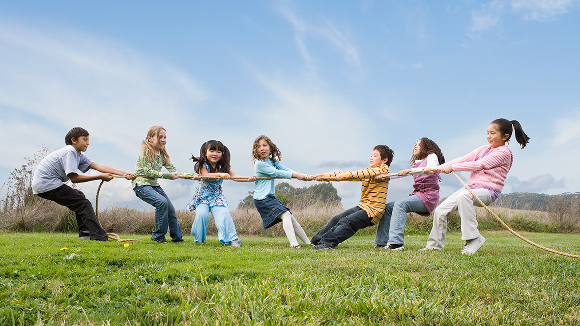 A group of children are playing tug of war. There are three children on the right side and four children on the left.